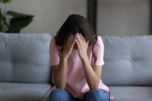 grieving woman sitting on couch holding head in hands