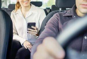 A passenger talks to her rideshare driver while holding her cell phone in New Jersey. If you have been in a rideshare accident, get medical help and contact a lawyer to help you recover financial compensation.